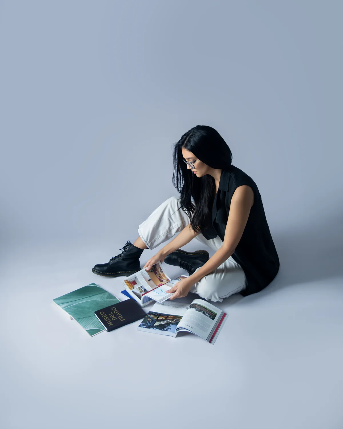 Elena Abarca, sentada en el piso, hojea libros y revistas de arquitectura.